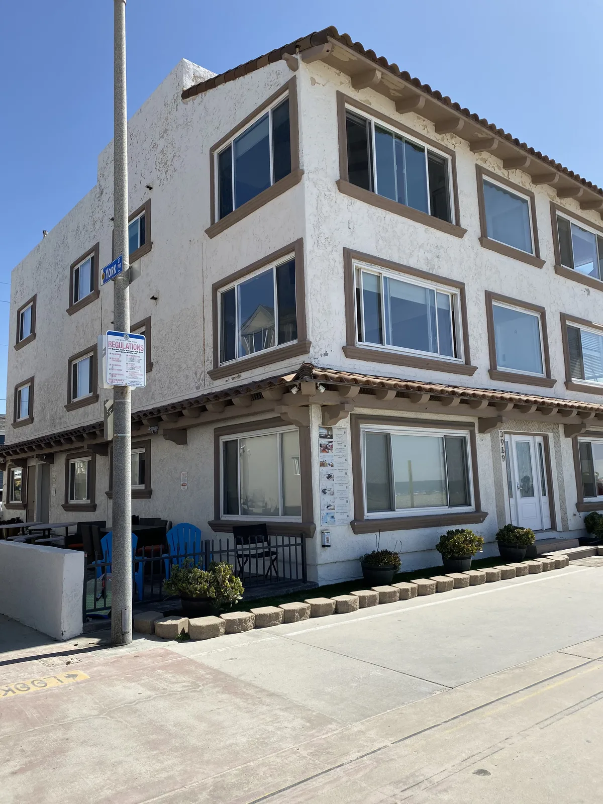 Weathered stucco with flaking finish and dated brown trim on a Pacific Beach corner building before refinishing